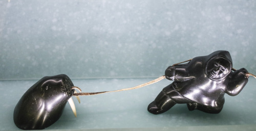 small statue depicting a hunter dragging the head of a walrus on a rope. Made of steatite, ivory, and leather