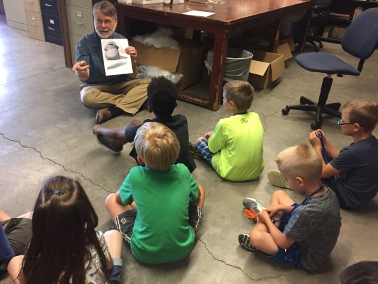 Researcher Tim Pearce sitting on the floor talking to a group of campers 