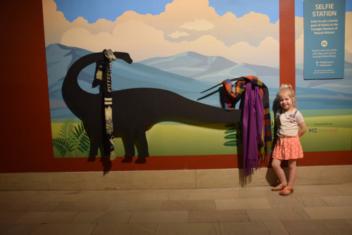 child posing with a dinosaur dressed up in scarves 