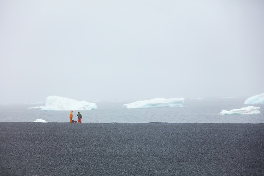two explorers in the distance on a flat, baren part of antartica