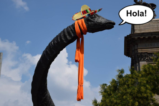 Dippy the dinosaur statue in a hat and scarf with a thought bubble that says Hola! 
