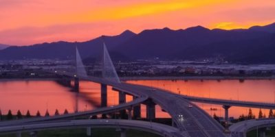 bridge over a river with mountains in the background at sunset