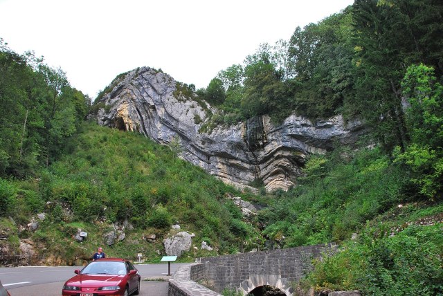 Car parked in front of rock formation that appears to have folds in it. 