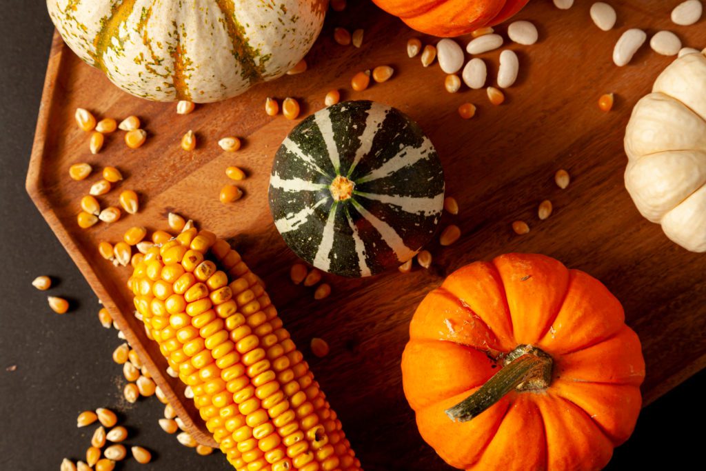 gourds, corn, and seeds on a wooden platter on a black counter