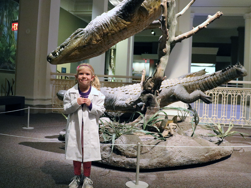 A girl scientist smiles in front of a crocodile diorama