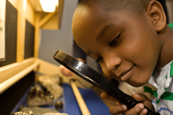 A young boy studies a mineral with a magnifying glass