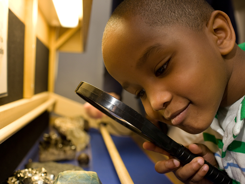 A young boy studies a mineral with a magnifying glass