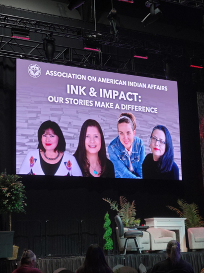 slide above a stage that has a photo of four people and the words: Associtation on American Indian Affairs, Ink & Impact: Our Stories Make a Difference