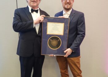 two people posing for the camera holding a framed award