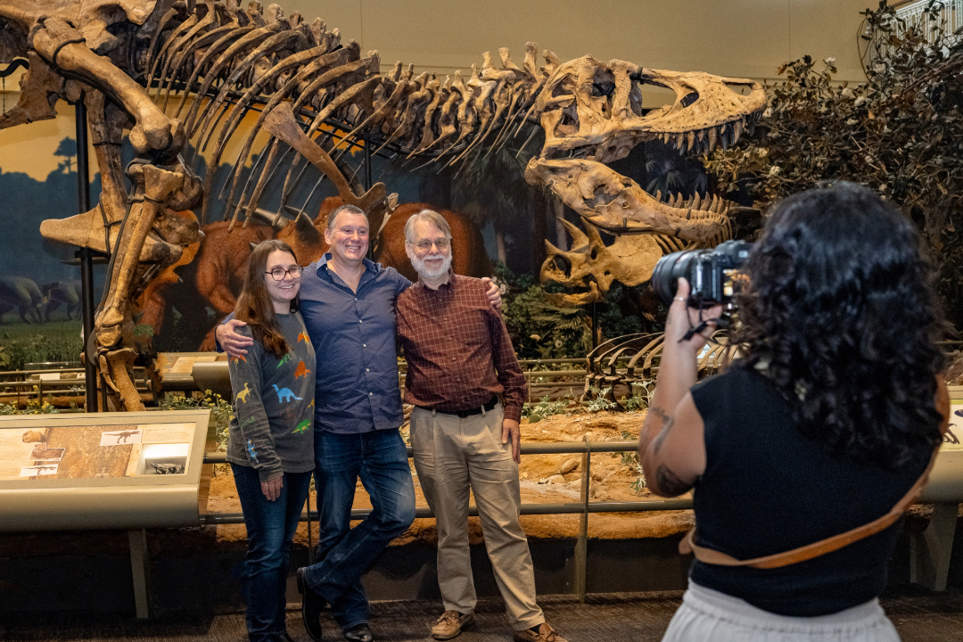 people posing for a photo in front of a T. rex